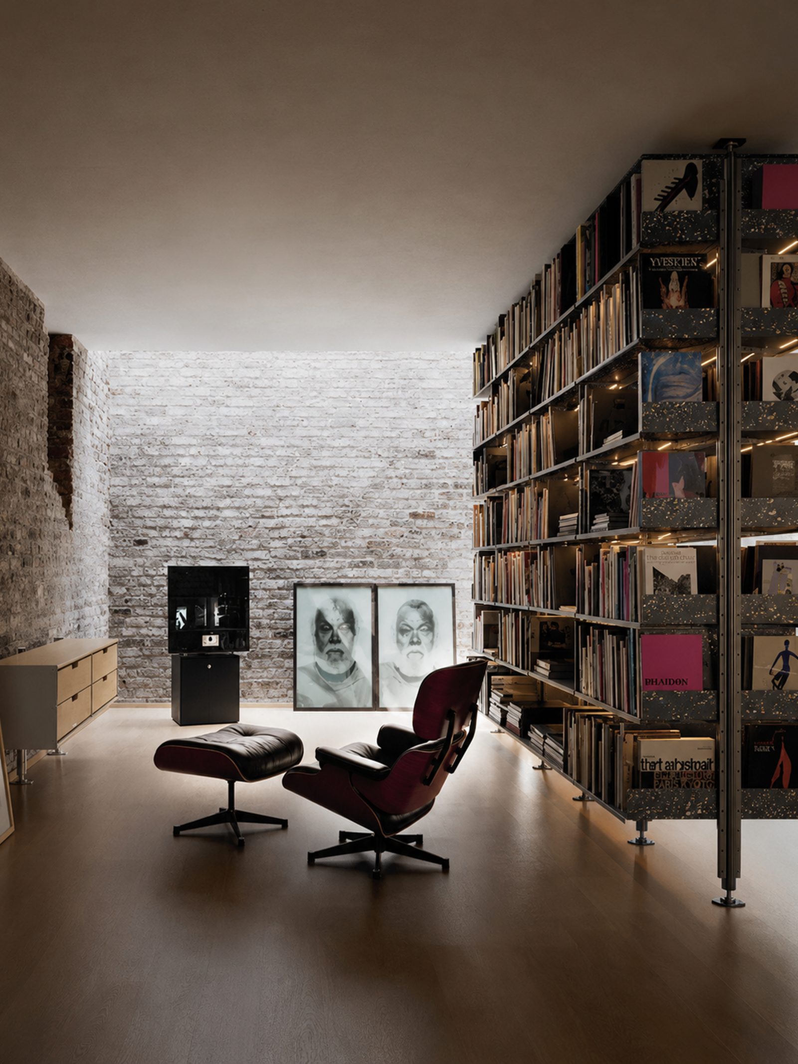 Quiet interior with exposed brick, Eames lounge chair and a full-height library of art books